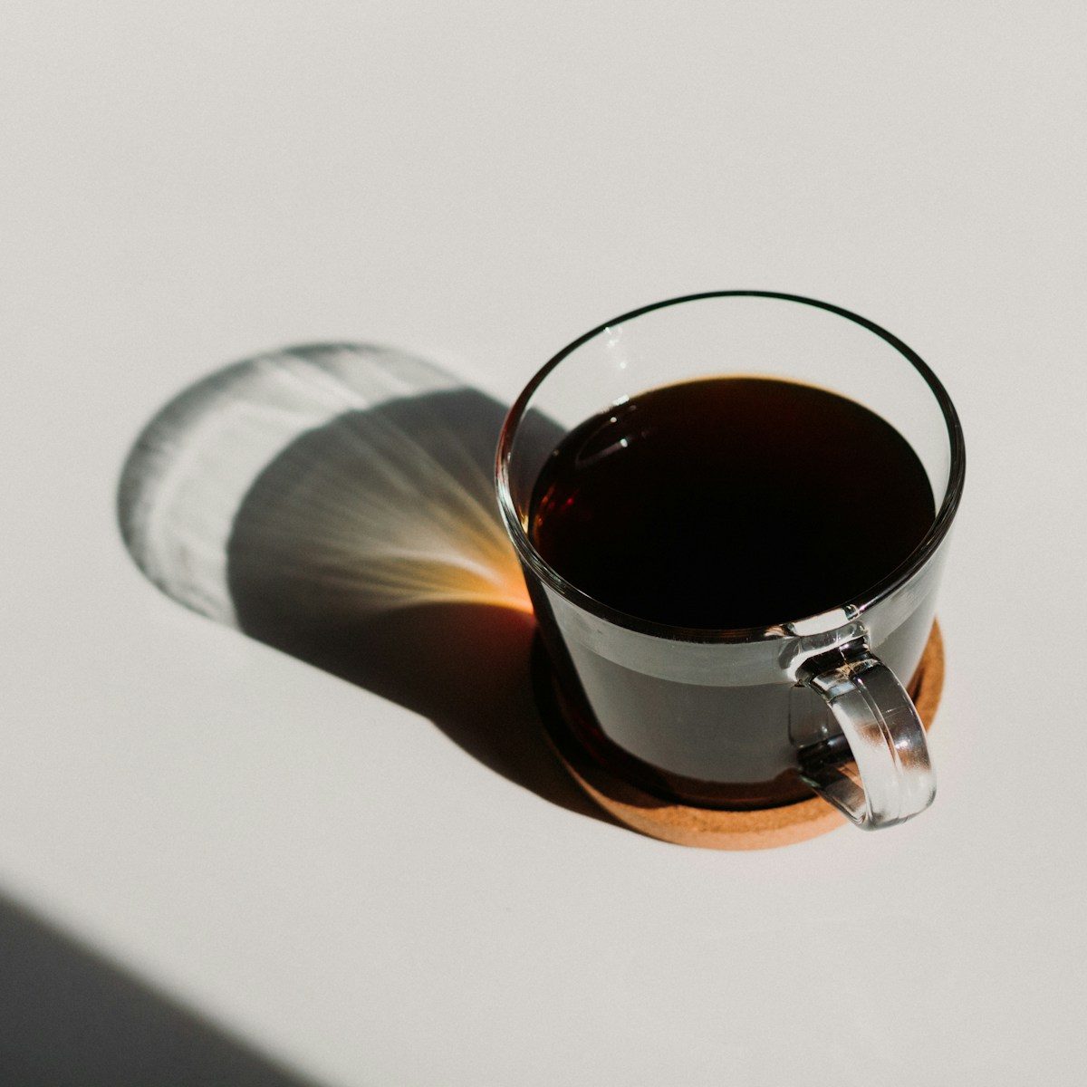 A small espresso machine on a clean kitchen counter, mid-pull, dark espresso flowing into a glass shot pitcher with a thick golden crema rising on top.