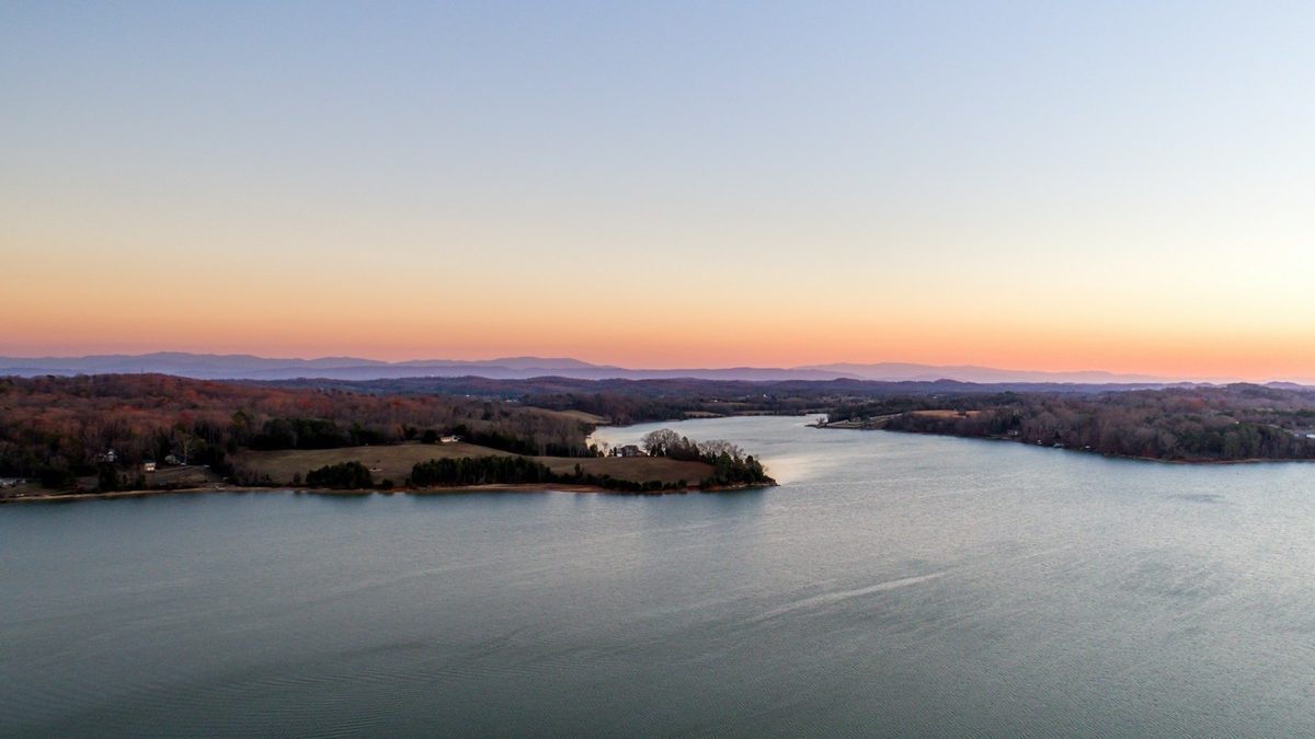 Aerial view of a wide East Tennessee lake at dusk — teal water winding between wooded points toward a mountain ridgeline on the horizon.