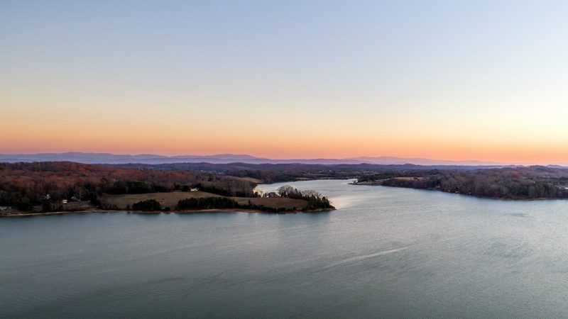 Aerial view of a wide East Tennessee lake at dusk — teal water winding between wooded points toward a mountain ridgeline on the horizon.