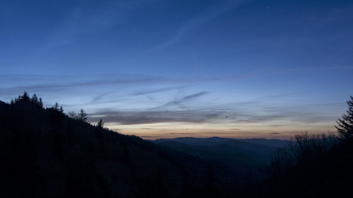 A predawn vista from the Oconaluftee Valley Overlook in Great Smoky Mountains National Park — layered Smoky Mountain ridges silhouetted against a soft band of orange sunrise.