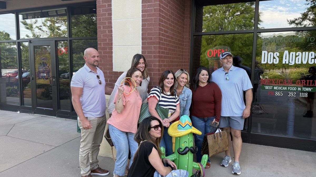 Hilary Kilgore and a group of fellow Knoxville REALTORS posing in front of the Dos Agaves Mexican Grill storefront for Cinco de Mayo, gathered around a green cactus statue wearing a sombrero, with the 'Best Mexican Food in Town' window decal visible behind them.