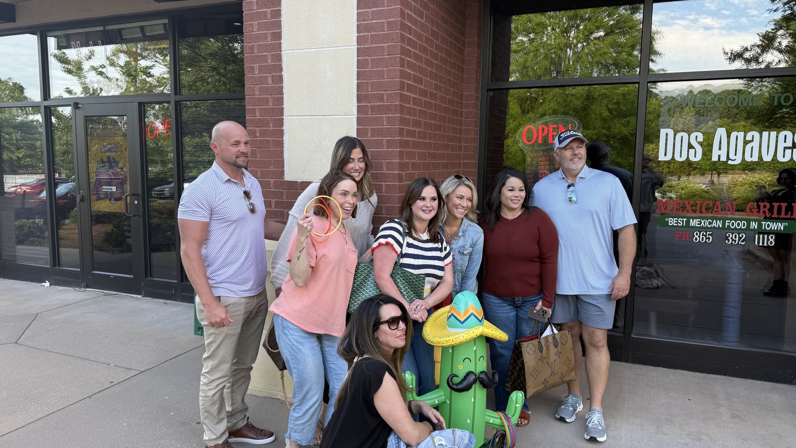Hilary Kilgore and a group of fellow Knoxville REALTORS posing in front of the Dos Agaves Mexican Grill storefront for Cinco de Mayo, gathered around a green cactus statue wearing a sombrero, with the 'Best Mexican Food in Town' window decal visible behind them.