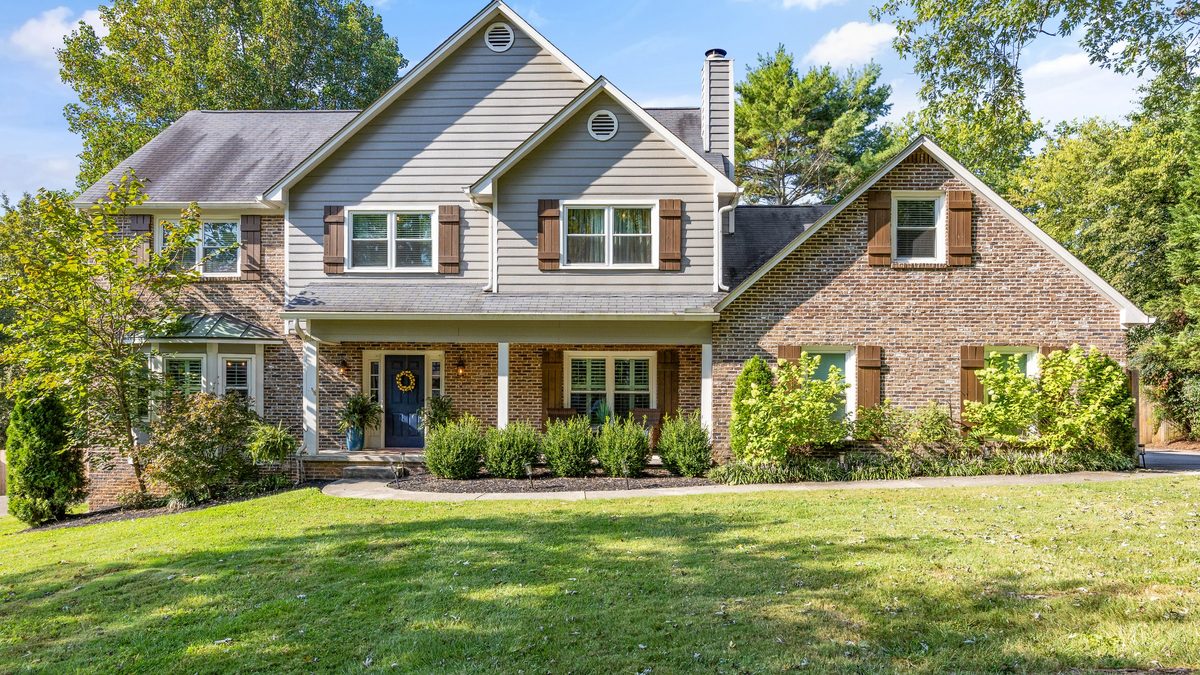 A two-story Farragut home with a brick first floor, lap siding above, board-and-batten shutters, and a deep green front lawn under mature trees.
