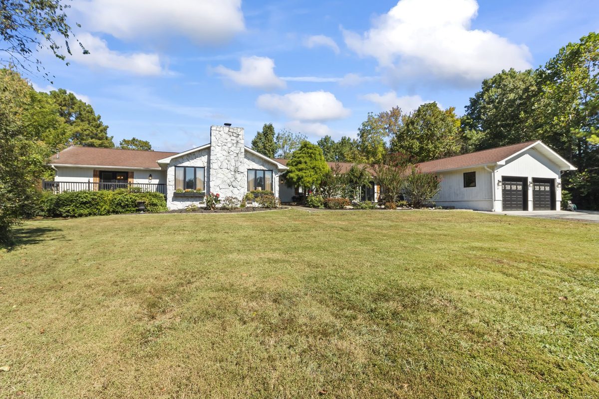 A white board-and-batten ranch home with a stone chimney and a wide front lawn under tall trees on Westland Drive.