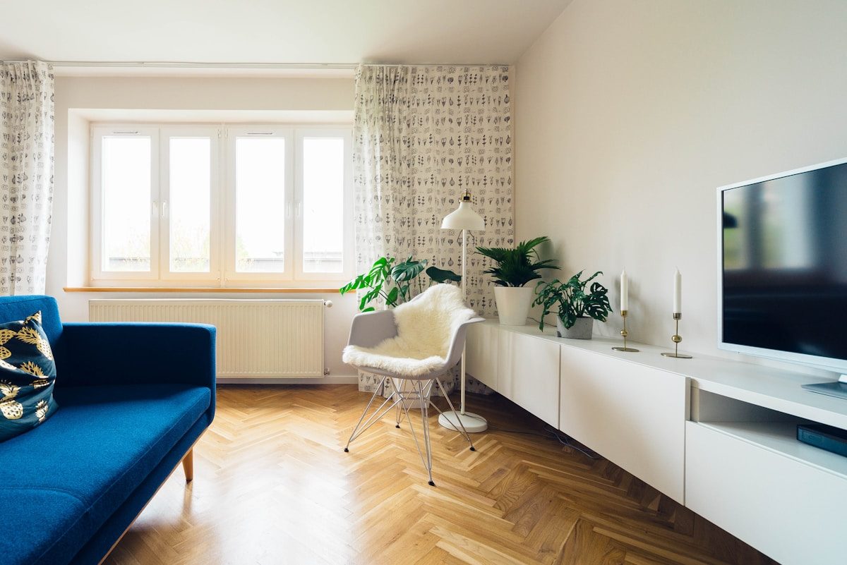 A bright, neutral living room with a linen sofa, sage throw pillows, and a vase of greenery on a wood coffee table — the kind of staging that helps a buyer picture themselves moving in.