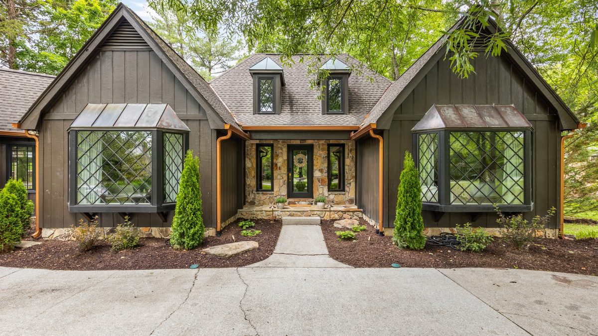 A spring-staged front entry of a red brick traditional West Knoxville home with a teal front door, a clay pot of mums, and dogwoods in early bloom — the first impression a buyer reads before they ever step inside.