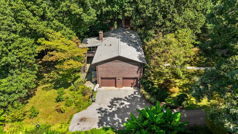 Aerial view of the brick home, side-entry basement garage and heavily wooded 0.41-acre lot